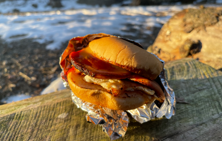 En Falukorvsburgare med ägg på en träyta, med snö i bakgrunden.