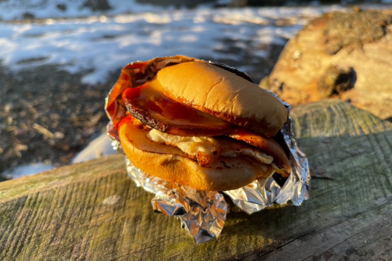 En Falukorvsburgare med ägg, placerad på en träyta med snö i bakgrunden.