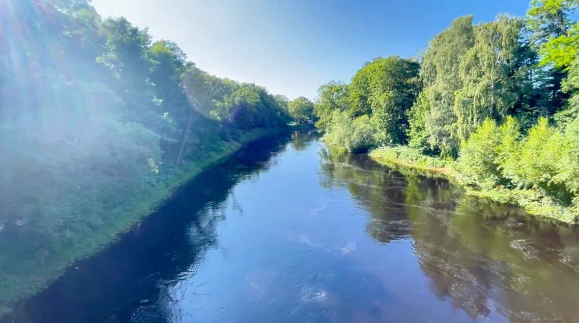 Ätran vid Vallarnas Friluftsteater Lugn flod omgiven av gröna träd under klart blå himmel.