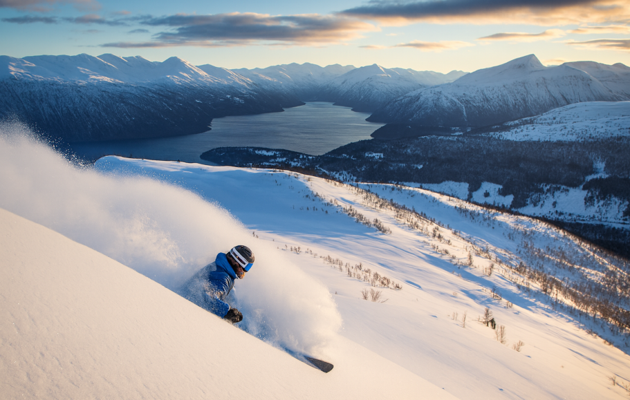 Illustration av Skidåkare i snöig terräng med fjäll och sjö i bakgrunden.