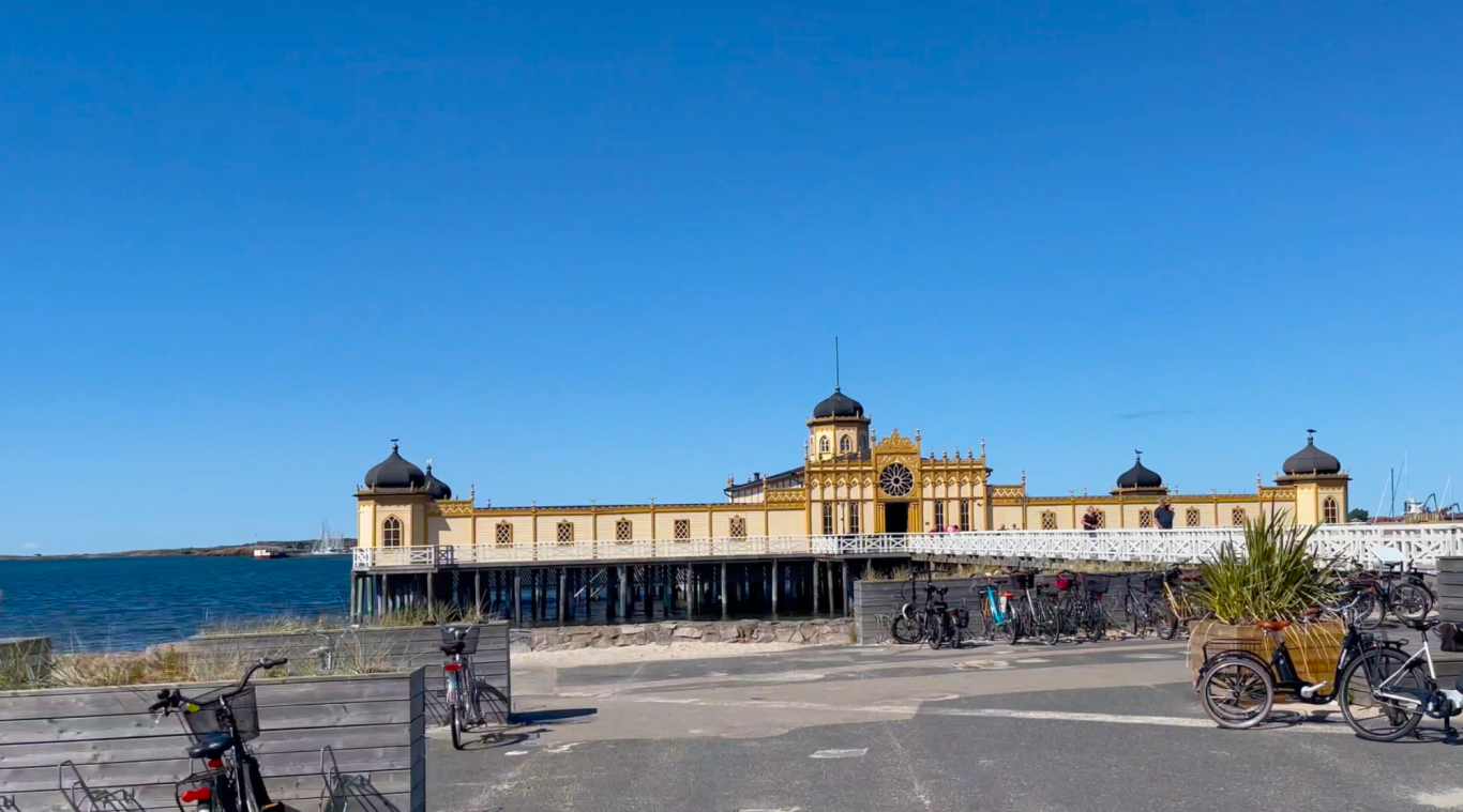 Varbergs Havsbad En gammal brygga vid havet med två torn, blå himmel och cyklar i förgrunden.