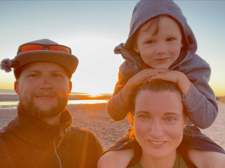 En man, en kvinna och ett barn på stranden vid solnedgången.