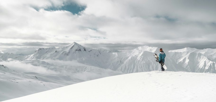 Person som går på snöklädd bergstopp under molnig himmel.