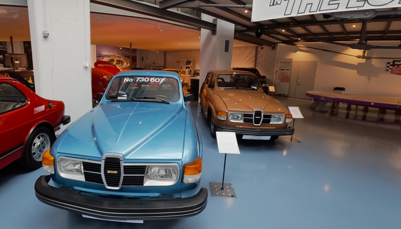 Saab 96 Två bilar i en utställning, en blå och en brun, med skyltar under dem.