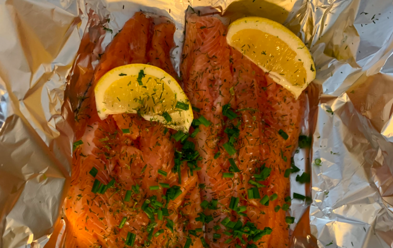 Grillad lax med citronskivor och grön känsla på aluminiumfolie.