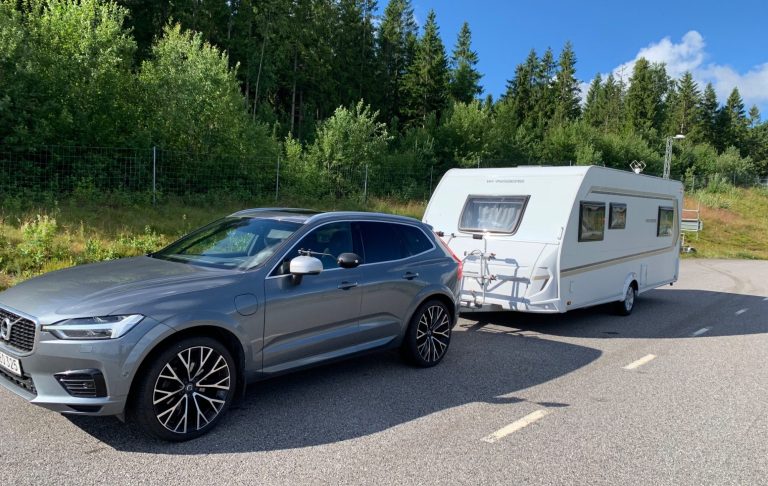 Grå SUV med släp parkerad vid en skogig väg.
