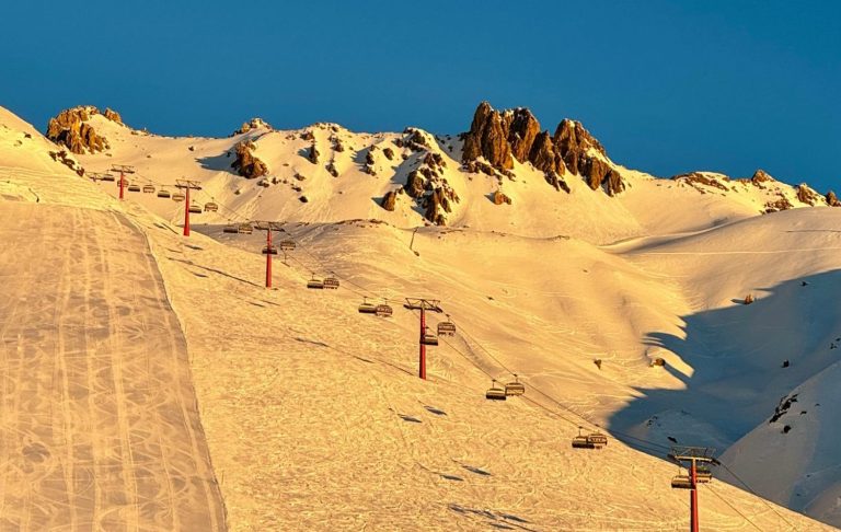 Snötäckta berg med skidbackar och stolslift, belysta av morgonsolen.