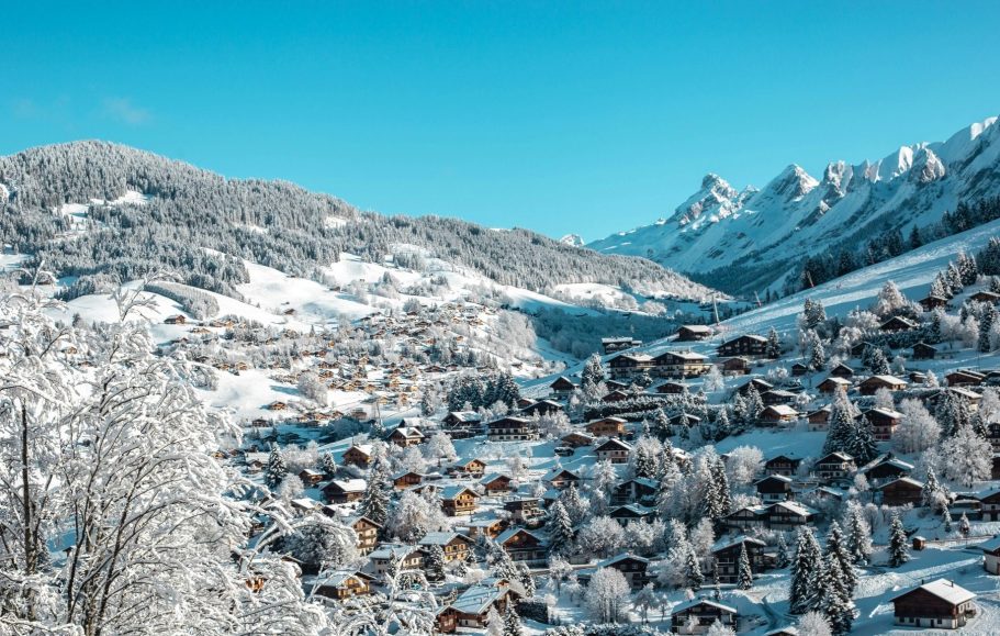 Vinterlandskap med snötäckta alpberg och alpby i dalgången under klarblå himmel.
