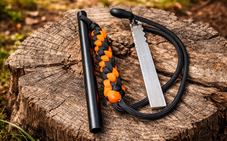 Eldstål och firestarter med paracord på ett trästycke i naturmiljö.