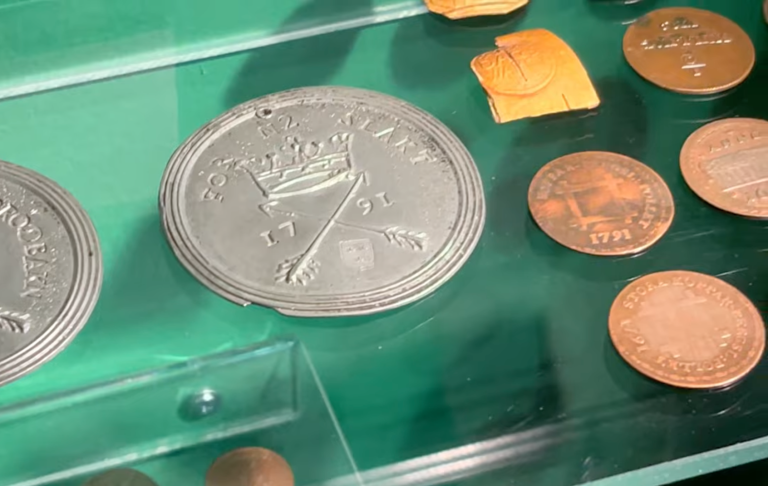 Ett antal mynt och en medalj som ligger på en grön yta.