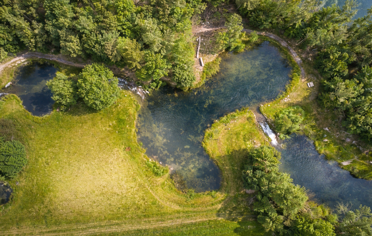 Grönskande natur med en slingrande bäck och klarblått vatten.