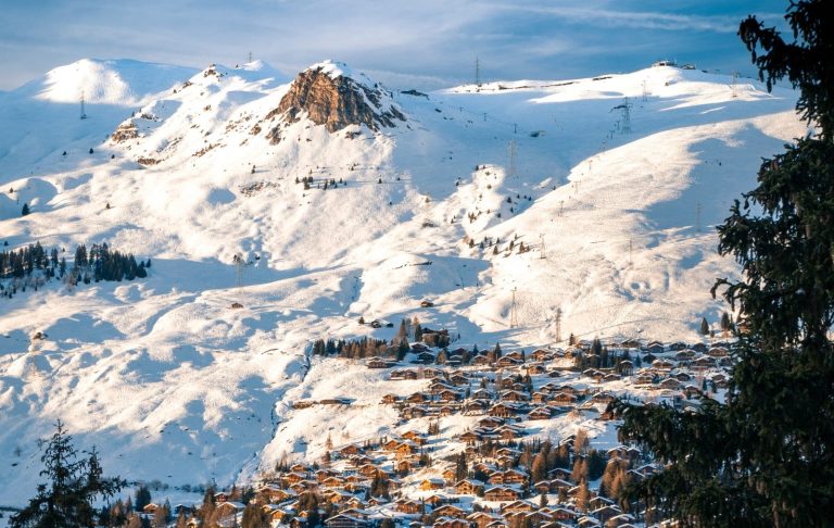 Snöklädda berg och en by i dalen under en klarblå himmel.