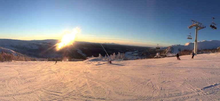 Vinterlandskap med snö, skidbackar och en solnedgång i bakgrunden.