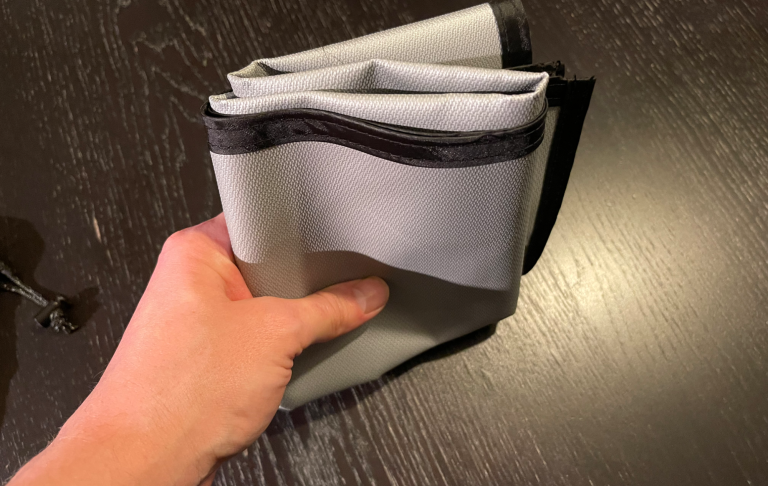 En hand som håller en vikbar, grå och svart plastförvaring.