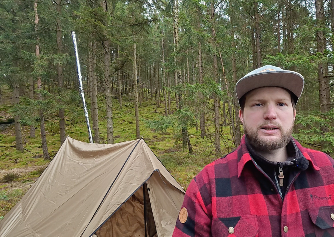 Johannes och Tältet En person står framför ett tält i en skog med tät vegetation.