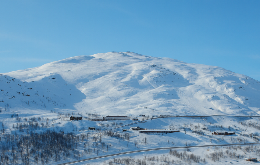 Illustration av Snöklädd bergslandskap med klarblå himmel och några byggnader i dalen.