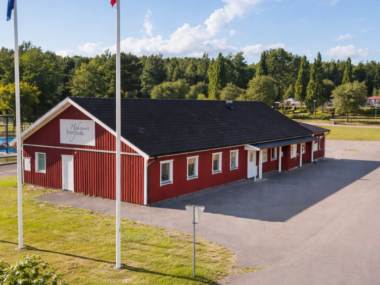 Röd byggnad med tak av platt tegel, belägen i en grönskande omgivning.