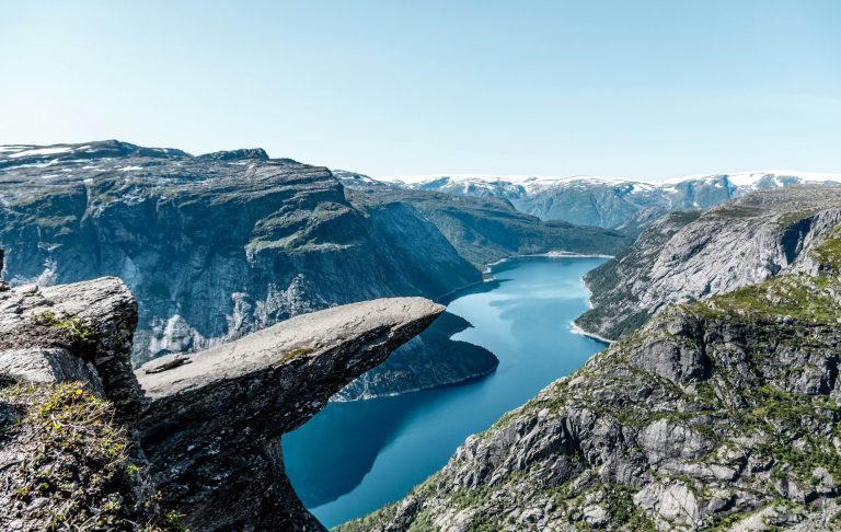 Utsikt över fjord med berg och klippor under klarblå himmel.