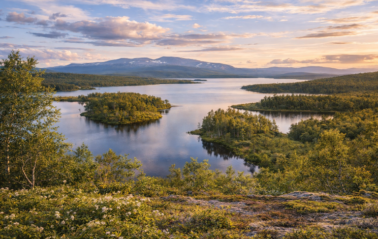 Vacker sjölandskap med öar, grönskande vegetation och fjärran berg i solnedgång.