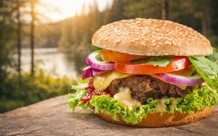 En saftig hamburgare med ost, grönsaker och sesamfranskt bröd, placerad i naturen.