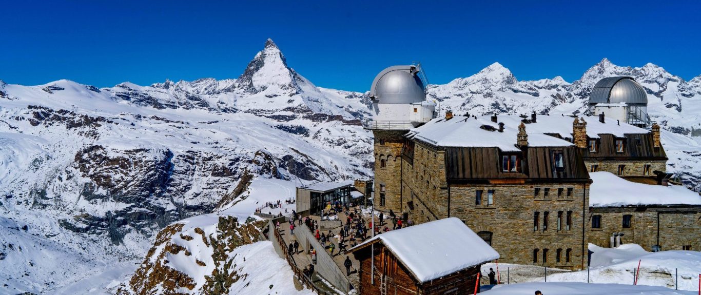 Vinterlandskap med snöklädda berg och en observatoriet i förgrunden. Matterhorn i bakgrunden.