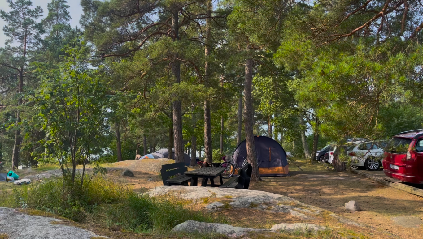Tältplatser och parkeringen Campingområde med tält och bilar omgiven av träd och natur.