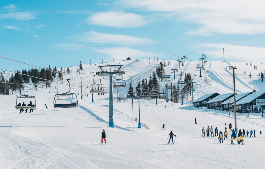 Skidbacke med liftar och åkare på snöklädda sluttningar under en klarblå himmel.