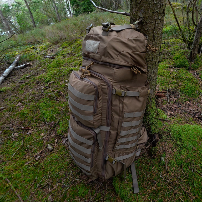 En frilufts ryggsäck En brun ryggsäck lutad mot ett träd i en grönskande skog.