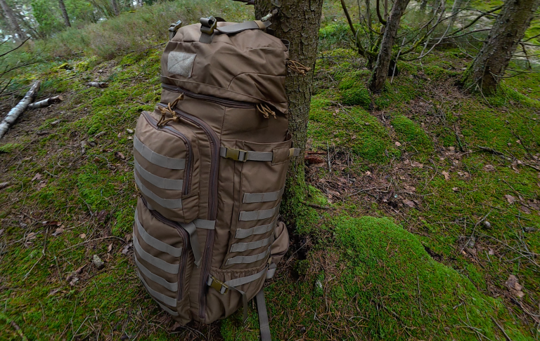 En brun ryggsäck lutad mot ett träd i en mossig skogsmiljö.