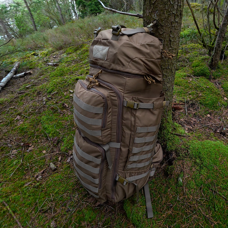 En beige ryggsäck lutad mot ett träd i en skog med grön mossa.