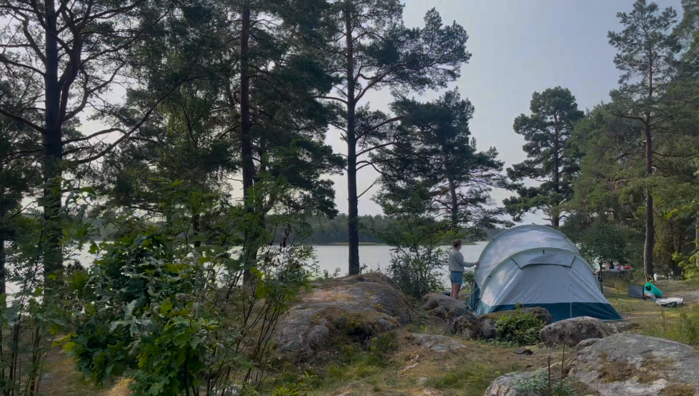 Tältområdet Tält vid en sjö omgiven av träd och stenar, med en lugn atmosfär.