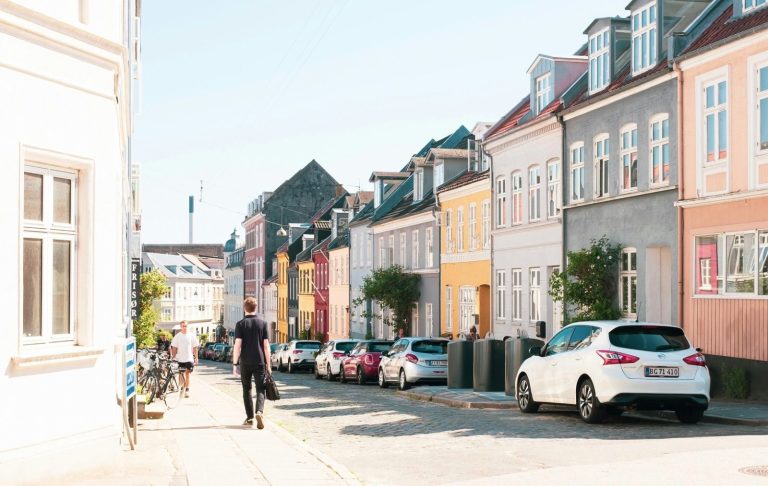 Brett gata med färgglada hus och parkerade bilar under en klarblå himmel.
