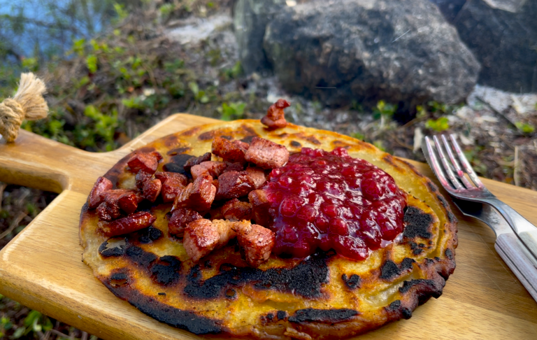 Blandad svensk pannkaka med bacon och rårörd lingonsylt på en skärbräda.