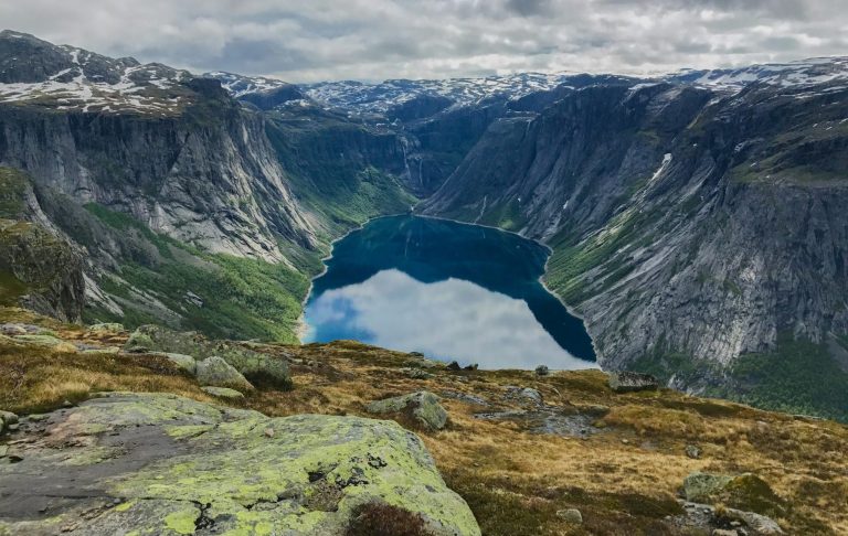 Havsdal med branta klippor och en sjö i dalen under molnig himmel.
