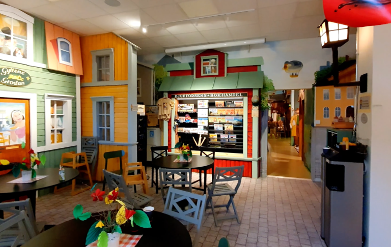 Färgglad inredning med bord och stolar, affärsdisk och väggar med husillustrationer.