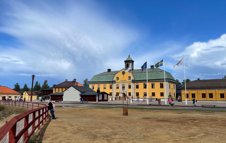 Gult historiskt byggnadskomplex med grön tak och blå himmel i bakgrunden.
