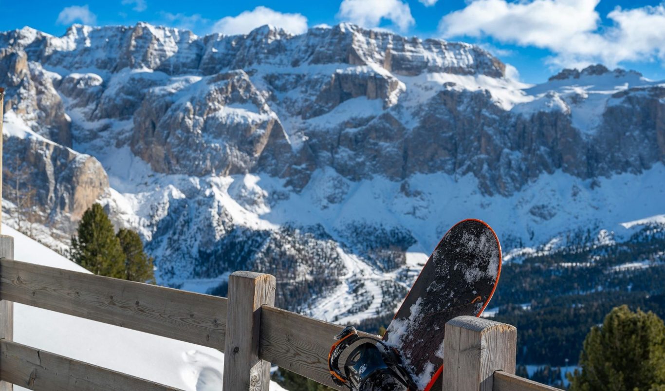 Snöbräda lutad mot ett staket med snötäckta alpberg i bakgrunden.