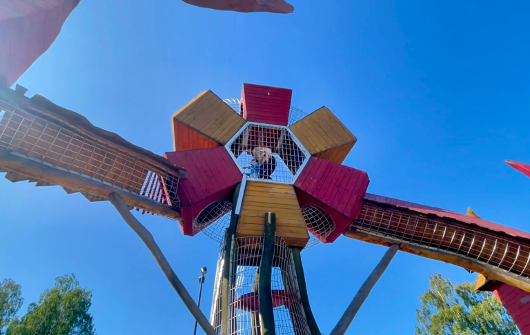 Lekplats med färgglada leksaker och en stor struktur under blå himmel.