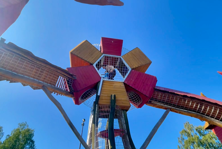 Lekplatsen på Vallarnas Friluftsområde Lekplats med färgglad struktur och en person som står på en plattform. Klara himmelska.