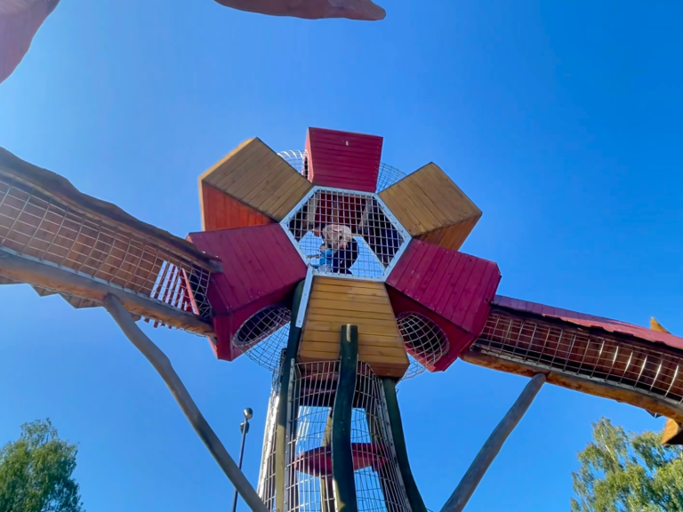Lekutrustning med en stor hexagonal struktur i trä och färgglada detaljer under blå himmel.