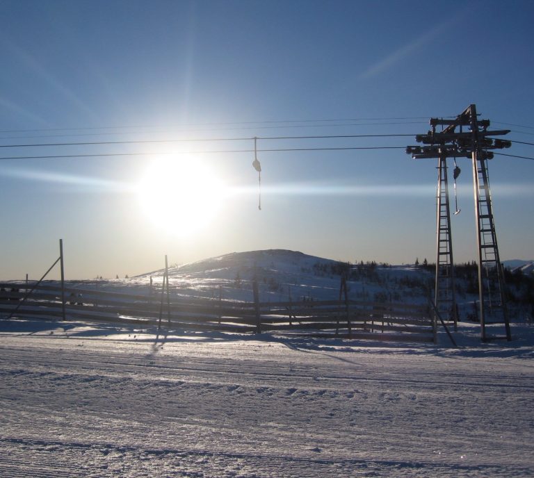Soluppgång över en snöbeklädd landskap med ankarlift och en kulle i bakgrunden.