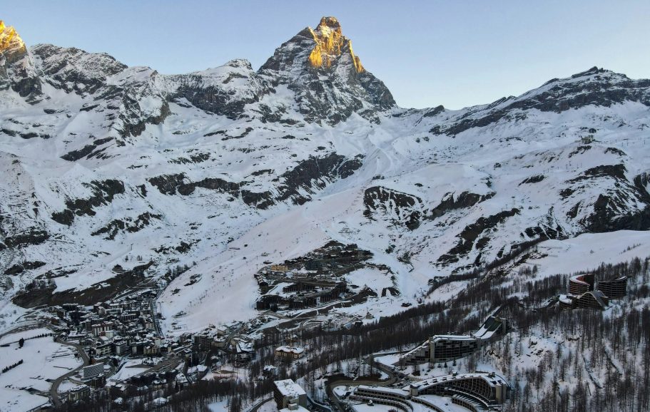 Snötäckta alpberg med en gyllene topp (matterhorn) i skymningen.