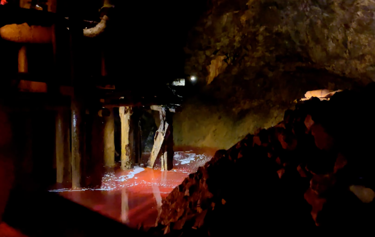 Gruva med rödaktig belysning och berg av grus i förgrunden.