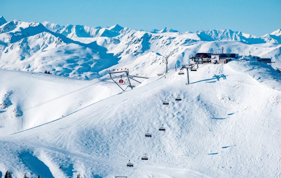 Snötäckta fjäll med skidliftar och en stuga i bakgrunden.