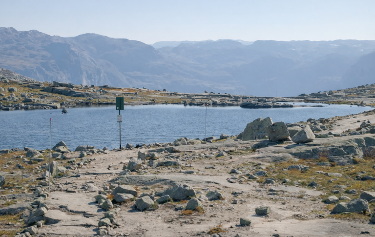 Landskap med en sjö omgiven av klippor och berg i bakgrunden.