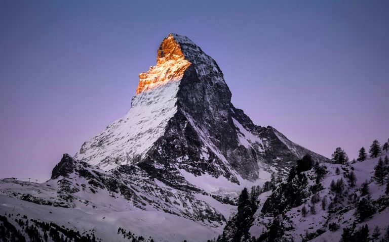 Matterhorn i skymning, delvis snötäckt med ett gyllene ljus på toppen.