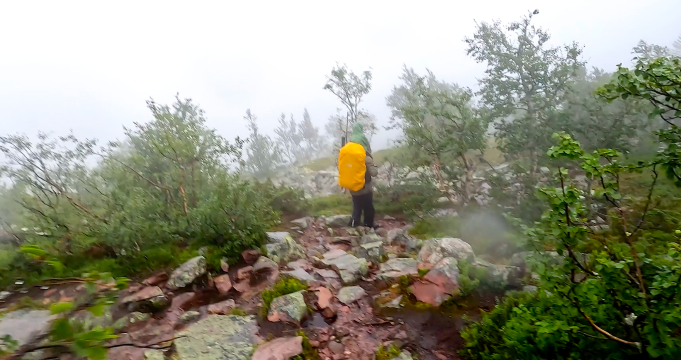 Spöregn och Åska i Fulufjällets Nationalpark Vandrare med gul ryggsäck på stenig stig i dimmig natur.