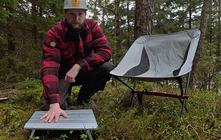 En man i rutig jacka testar en bärbar stol i skogen.