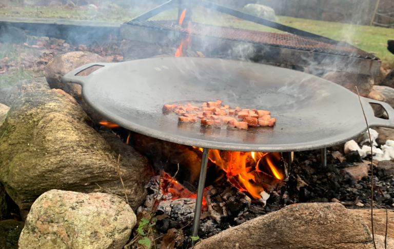 Köttsnuttar grillas på en stor platta över öppen eld omgiven av stenar.