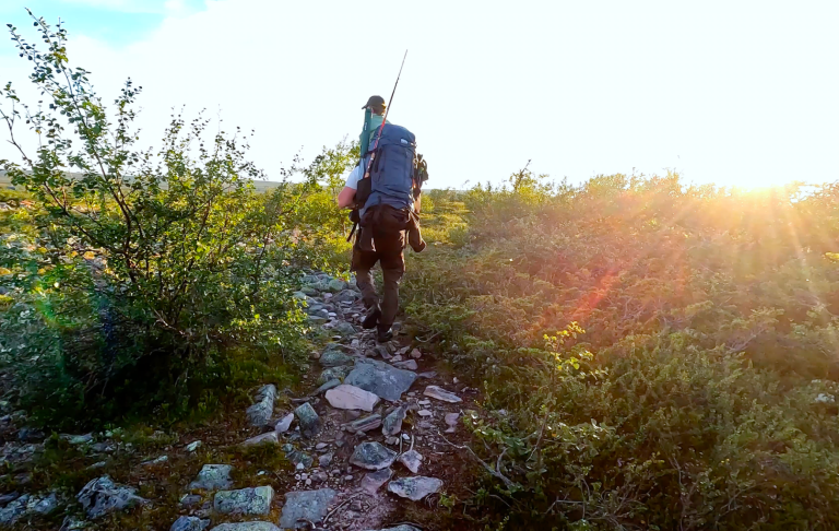 Vandrar längs en stenig stig med solnedgång i bakgrunden och grönska runtom.